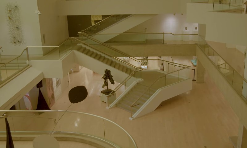 A quiet, warm-toned museum atrium with intersecting ramps, stairs, and glass railings